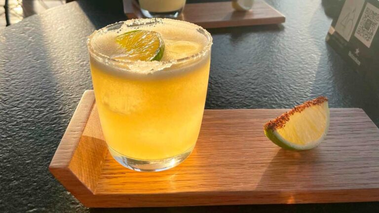 A glass of cocktail with lime on top and sugar on its glass rim