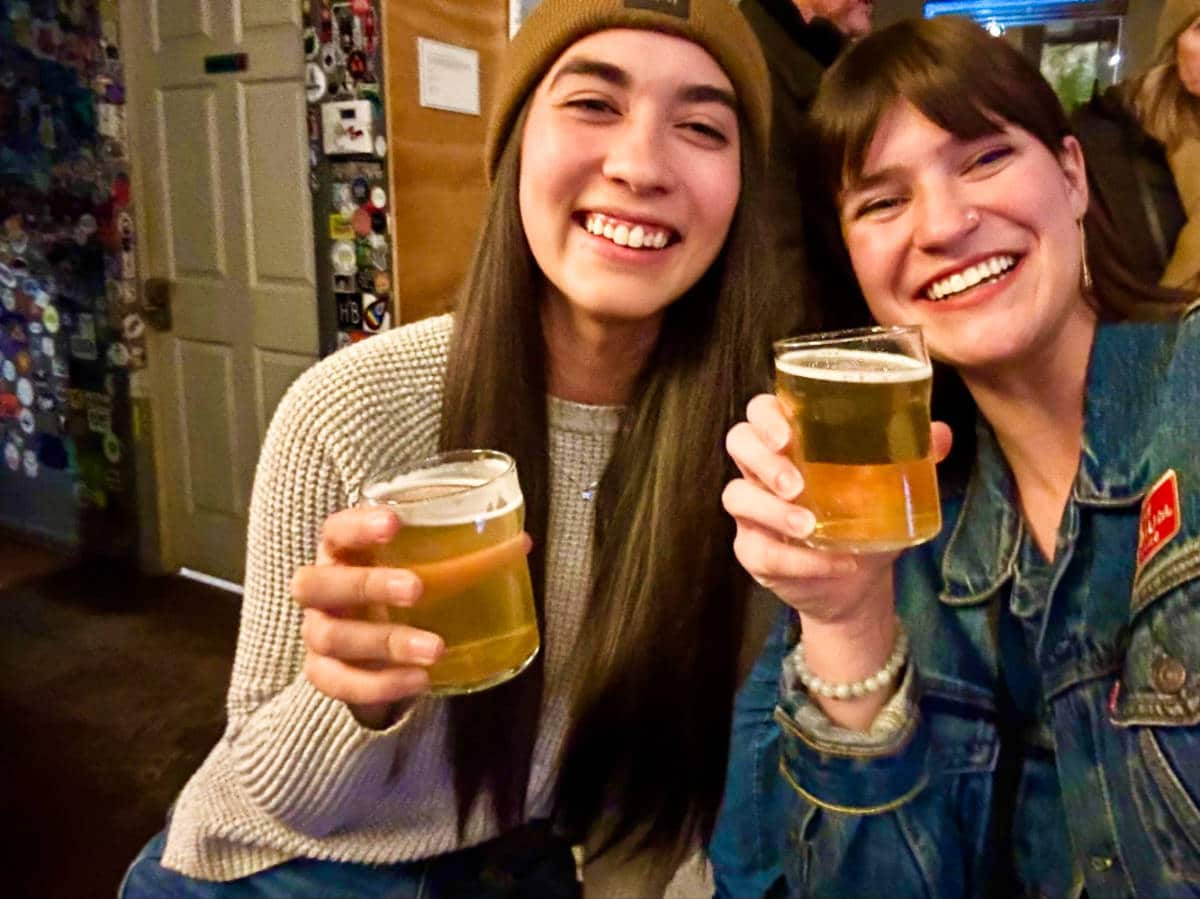 Travel Lemming editor Abigail Bliss with Betty Hurd posing while holding glasses of beer at Our Mutual Friend Brewing Company