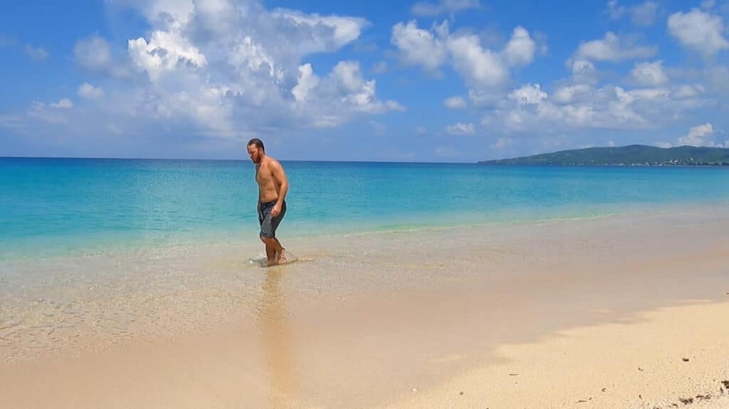 A man standing at the shallow turquoise blue water and white sand beach in USA