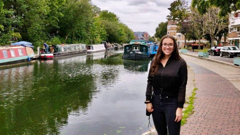 The author Brooke Horrobin posing near the river with boats floating on the river