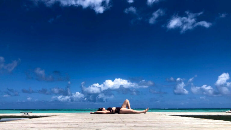 Author Claudicet sunbathing on the dock near Juanillo Grill & Beach Club under a clear blue sky