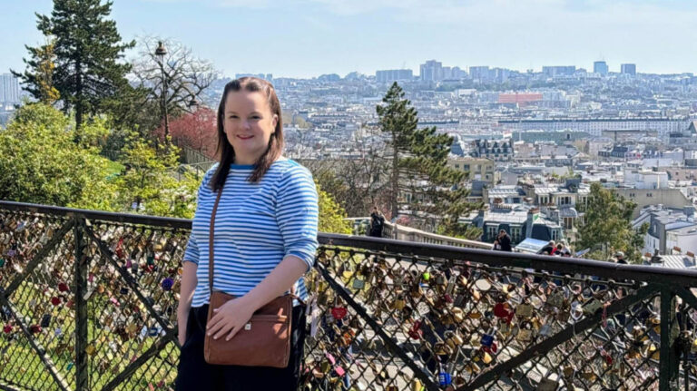 Author Rachel smiling in front of a love lock-covered fence at Square Louise Michel