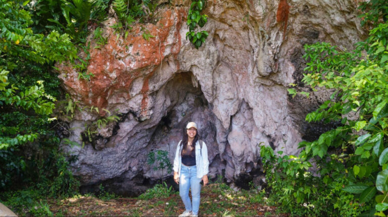 Author Vanessa smiling in front of a limestone cave surrounded by lush greeneries