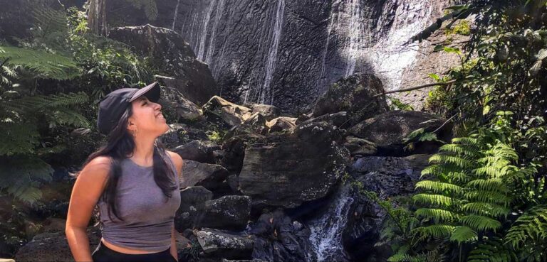 The author Vanessa Ramos posing for a photo in El Yunque with a waterfall on her background
