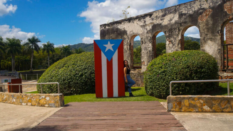 Author Vanessa standing next to the Puerto Rico Flag in Jardin Botanico y Cultural