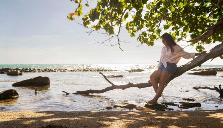 Author Vanessa sitting on a tree branch on a beach
