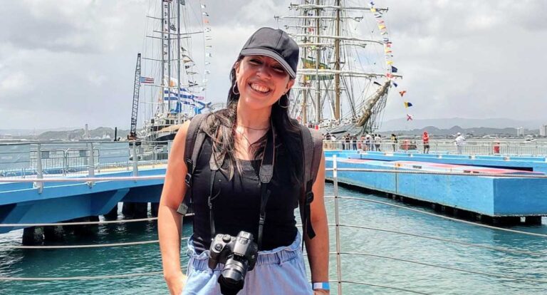 Author Vanessa Ramos smiling for a photo with sailing boats on the dock on her background