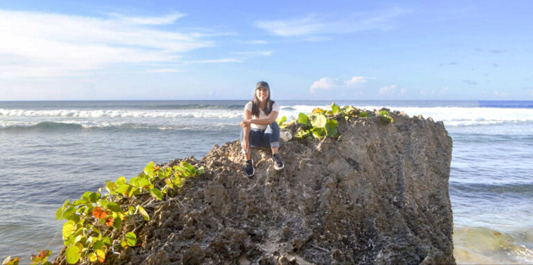 The author Vanessa sitting on a boulder stone near the beach