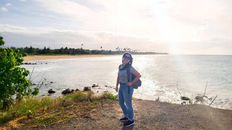 Author Vanessa stands on a rocky coastal path, with the ocean visible in the background