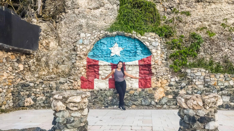 Author Vanessa stands in front of a stone wall painted with the Puerto Rico flag