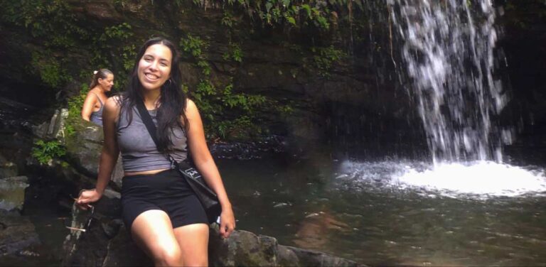 The author Vanessa Ramos sitting on a rock with a waterfall on her background in El Yunque