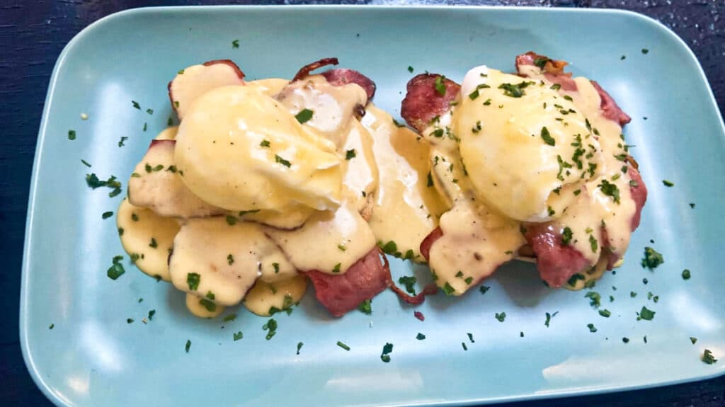 A turquoise blue plate with bacon eggs benedict topped with hollandaise sauce at Chairs and Coffee