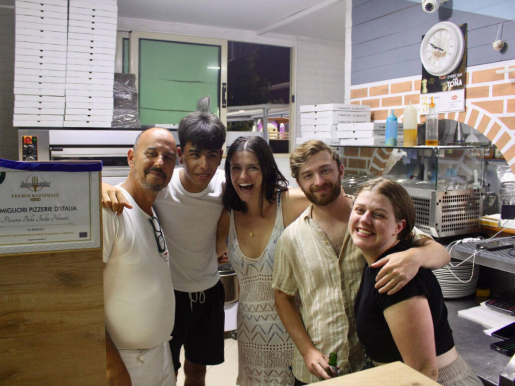 The author Betty Hurd and her friends smiling for a photo with the staff of the pizza place