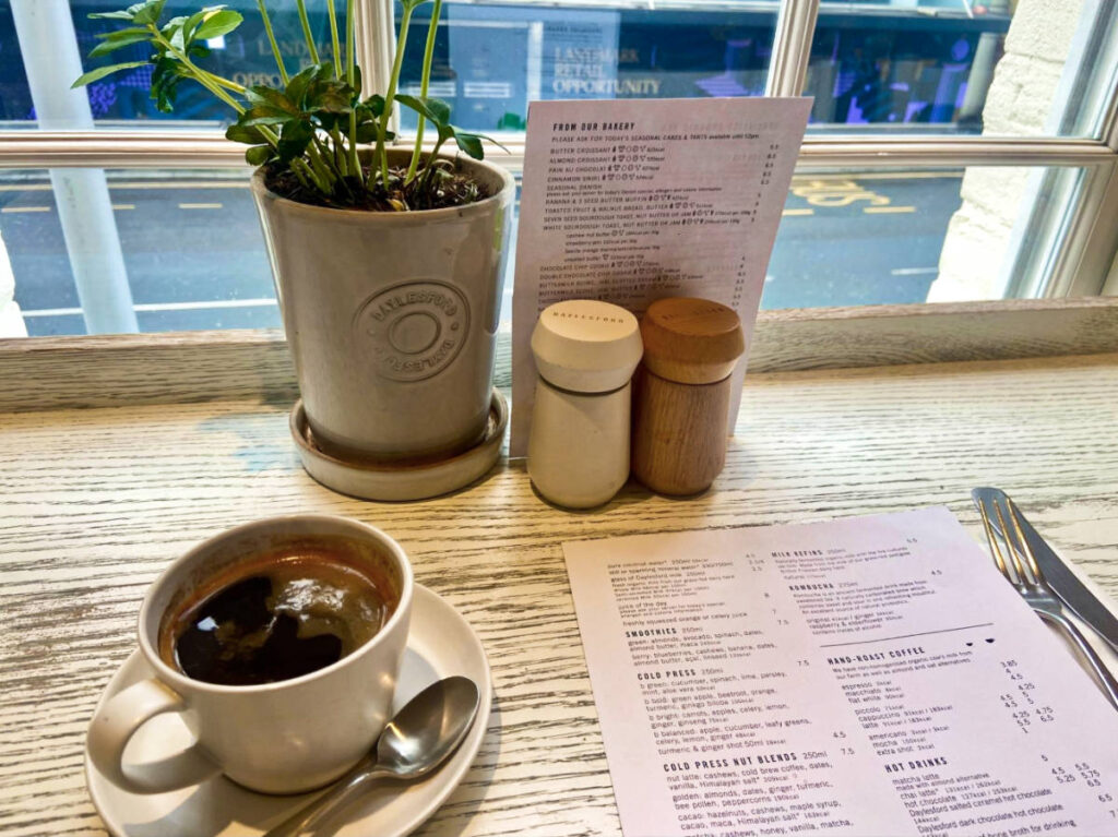 A cup of black Americano and menu by the window at Daylesford Organic