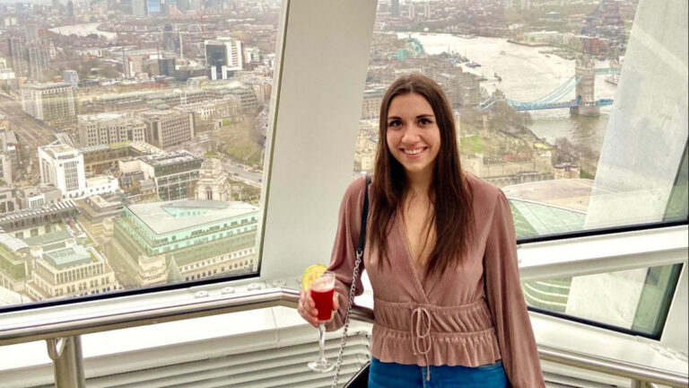 Brooke Horrobin, posing for a photo while holding a glass of drink with an overlooking view of the cityscape of London
