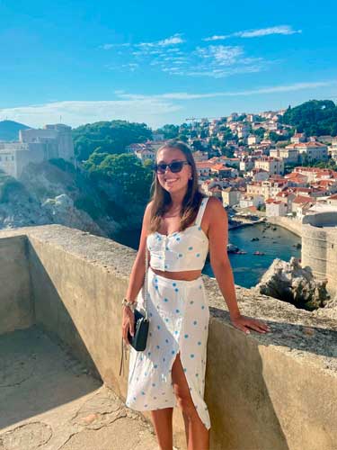 Brooke Horrobin smiling for a photo in Dubrovnik, Croatia and a scenic view on her background