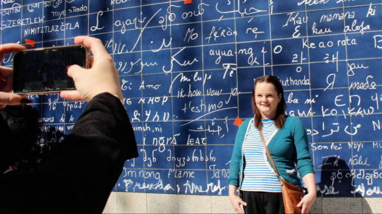 View of the hands taking a photo of Rachel Kapelke-Dale in front of the “I Love You” Wall