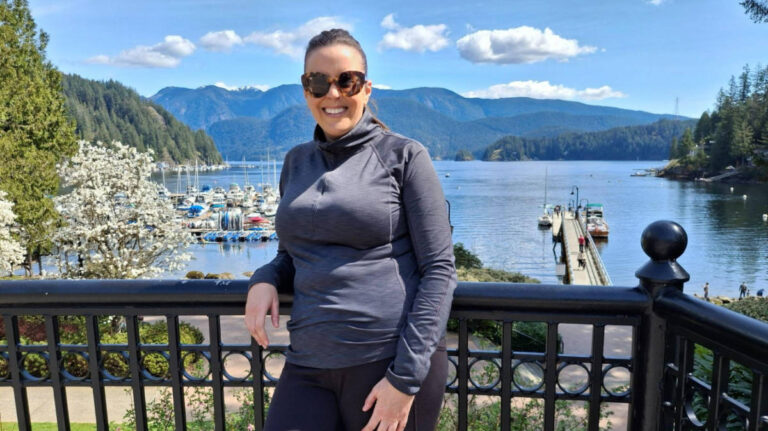 The author Catherine Driver posing for a photo with an overlooking view of the marina at Deep Cove