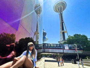 The author Chelsea Booker, posing in the Museum of Pop Culture with the Monorail and Space Needle in the background at Seattle Center