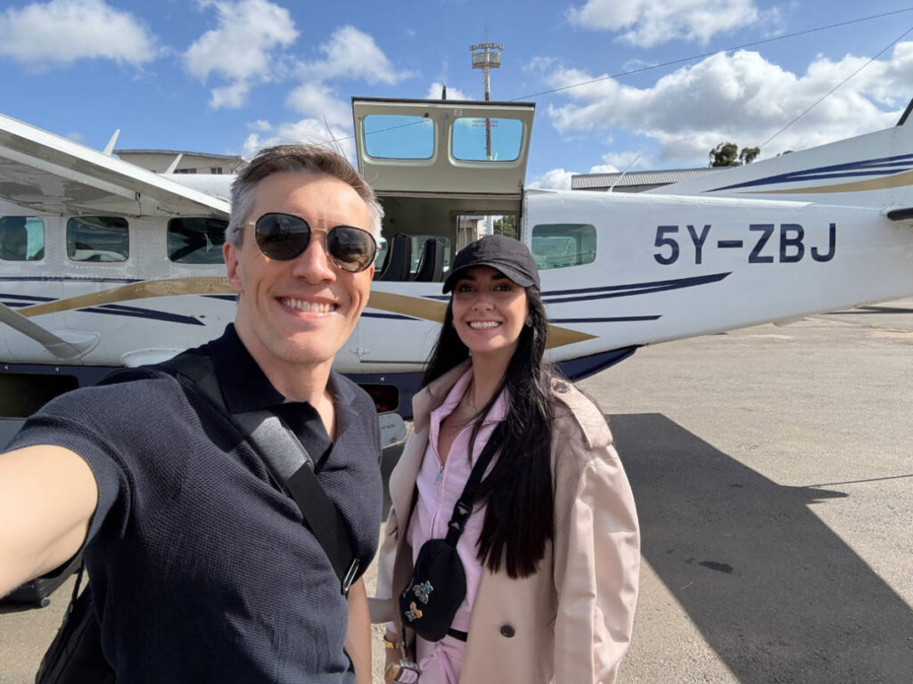 Travel Lemming founder Nate Hake and his partner Clara, smiling for a photo in front of the tiny Cessna