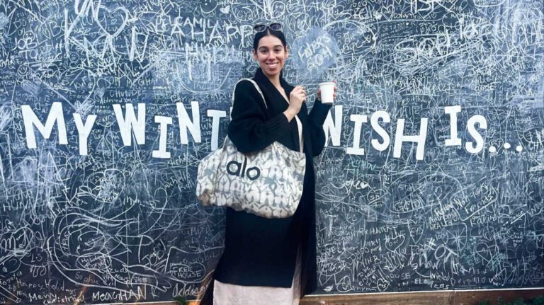 The author Claudicet Pena posing for a photo in front of The Winter Wish Wall
