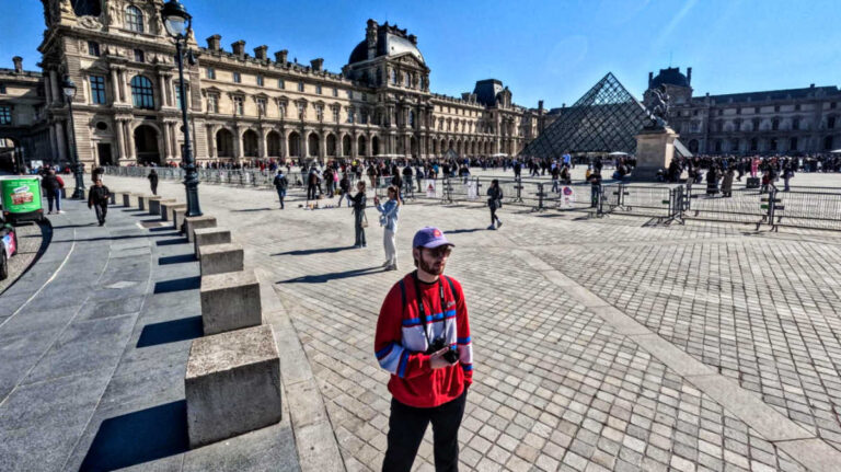 A man posing for a photo with the crowd wandering around the Louvre Museum