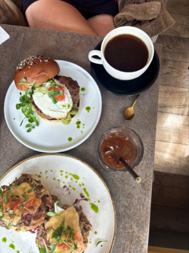 A plate with grilled halloumi, poached eggs & avo on toast and other plate with eggs benedict and drinks at The Farmer’s Mistress