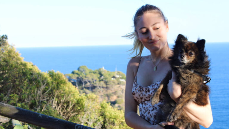 Travel Lemming Writer Sky Ariella and her dog, Bear, posing with a scenic overlooking view in Tossa De Mar, Spain