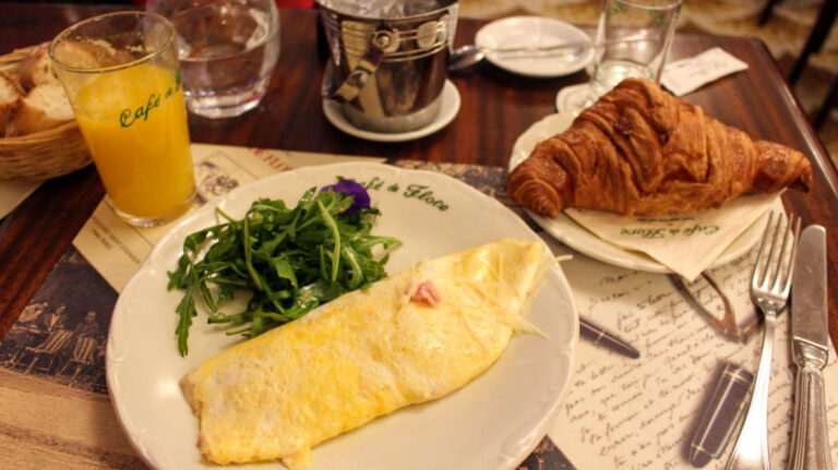 Ham and cheese omelette with arugula, a croissant on a side plate, a glass of orange juice