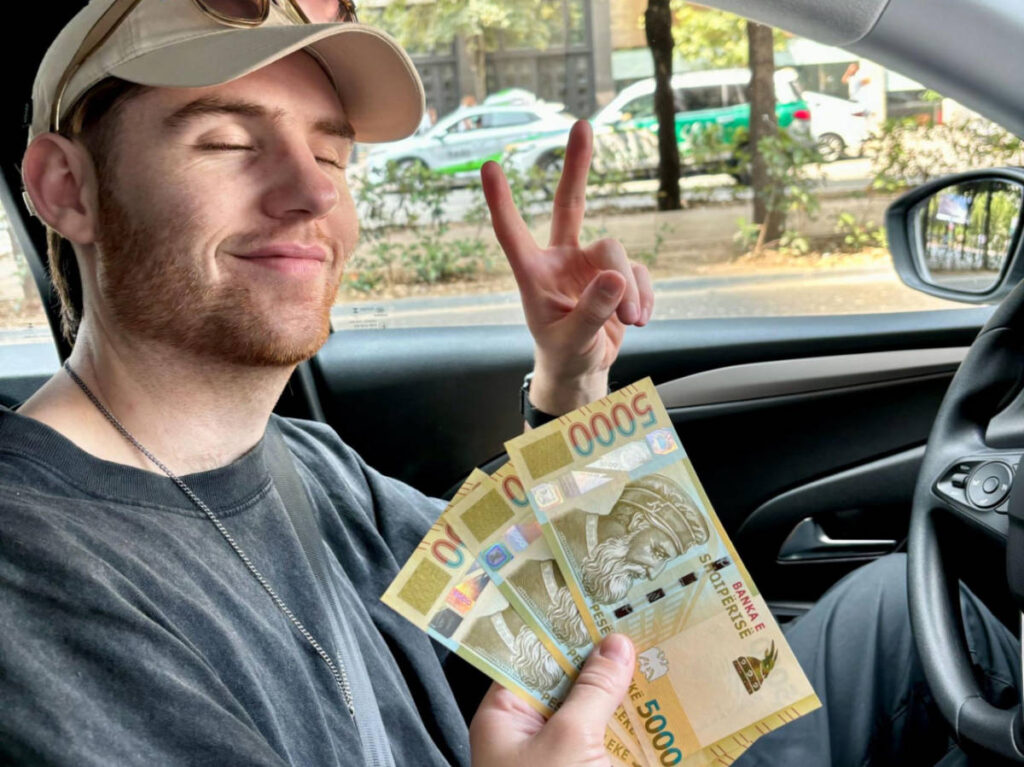 A man smiling for a photo with a handful of leks in front of him