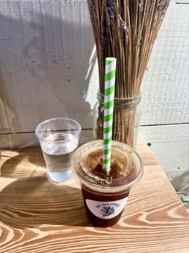 A to-go cup of iced Americano with straw and a cup of water on a wooden table