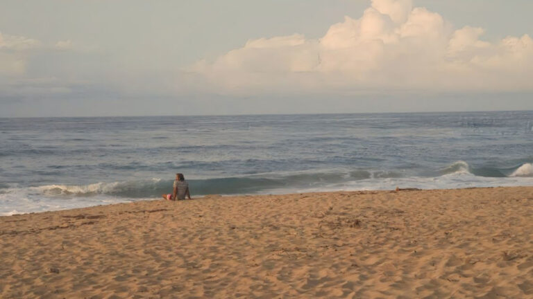 A man sitting along the sandy beach at sunset