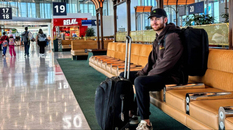 A man sits in a Terminal of Paris Charles de Gaulle Airport, with his backpack and suitcase beside him