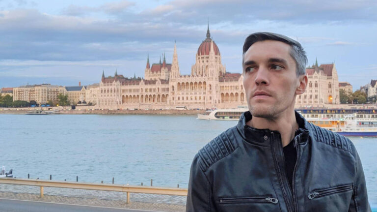 Travel Lemming founder, Nate Hake, posing for a photo near the river with the Parliament Building in the background