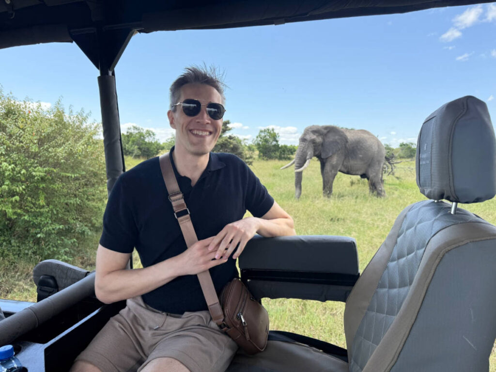 Travel Lemming founder Nate Hake, smiling for a photo on the vehicle with the huge elephant in the background