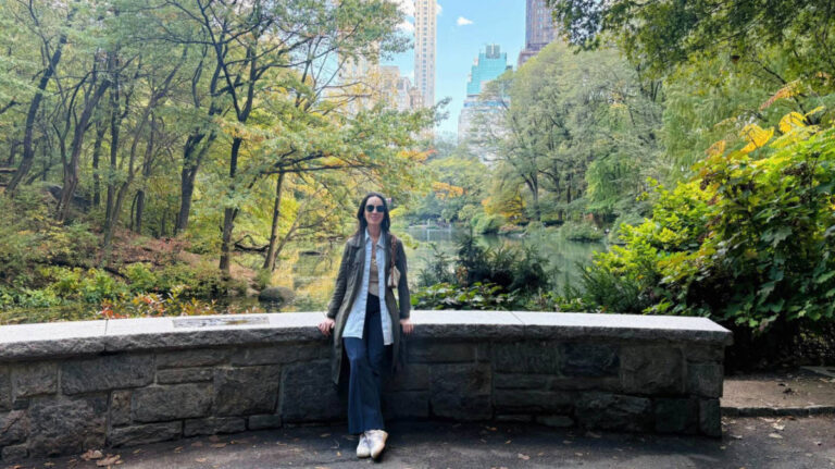 The author Niamh Hayes, sitting on a ledge wall with skyline views in the background surrounded by greenery