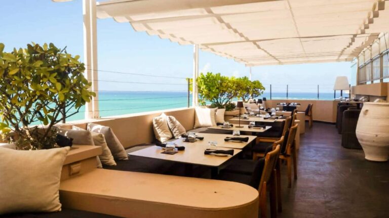 An oceanfront dining area with tables and chairs, offering views of the sea