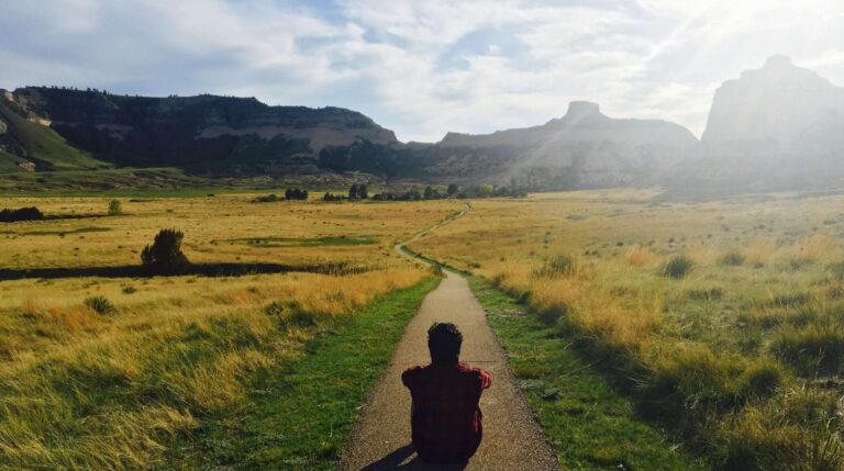 A person sitting on a path in the middle of an open field
