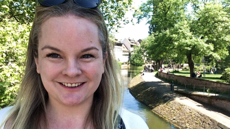 The author, Rachel Kapelke-Dale smiling for a selfie at a canal in La Petite France