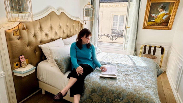 The author Rachel Kapelke-Dale sitting on a bed on a hotel in the 6th Arrondissement