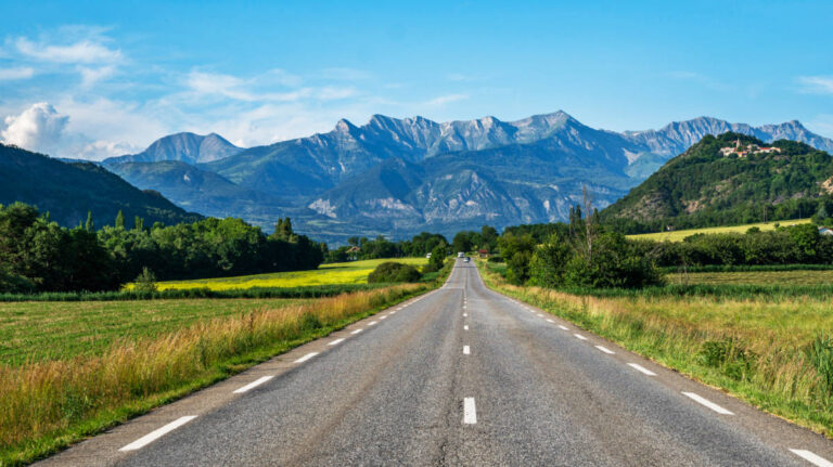 A long straight road leading towards the picturesque mountain views in France