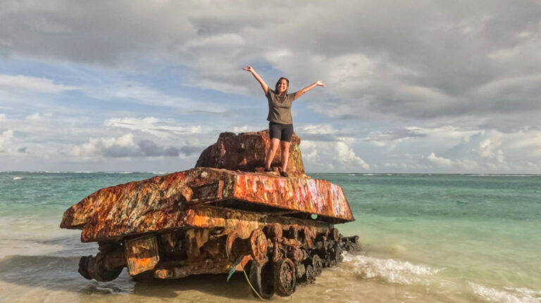 The author Vanessa Ramos on top of a rusty tank on a shoreline