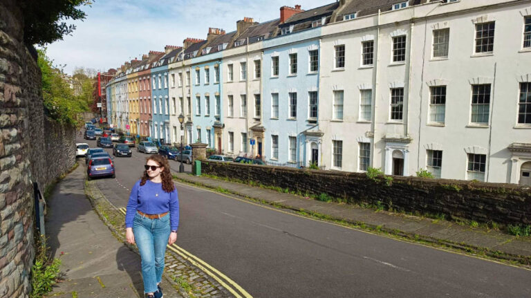 The author Ruthie Walters walking across the street with the colorful buildings in the background in Clifton