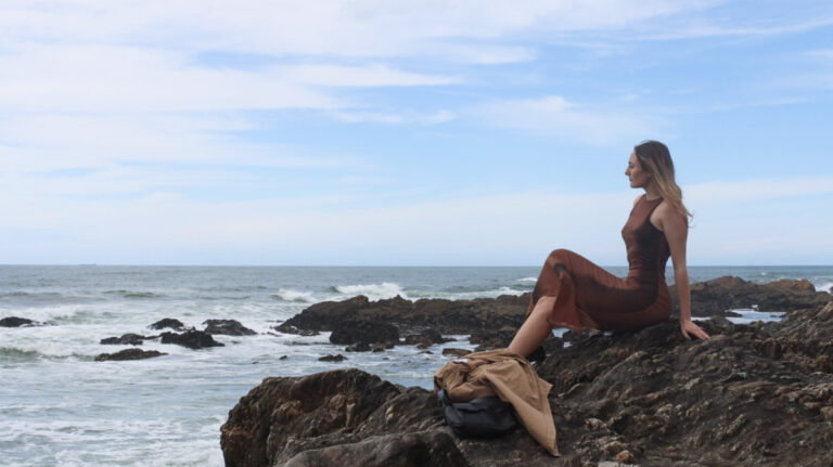 The author Sky Ariella enjoying the beach while sitting on the rock in Portugal
