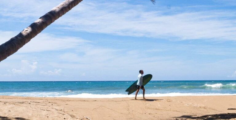 A man walking along the shoreline while carrying a surf board