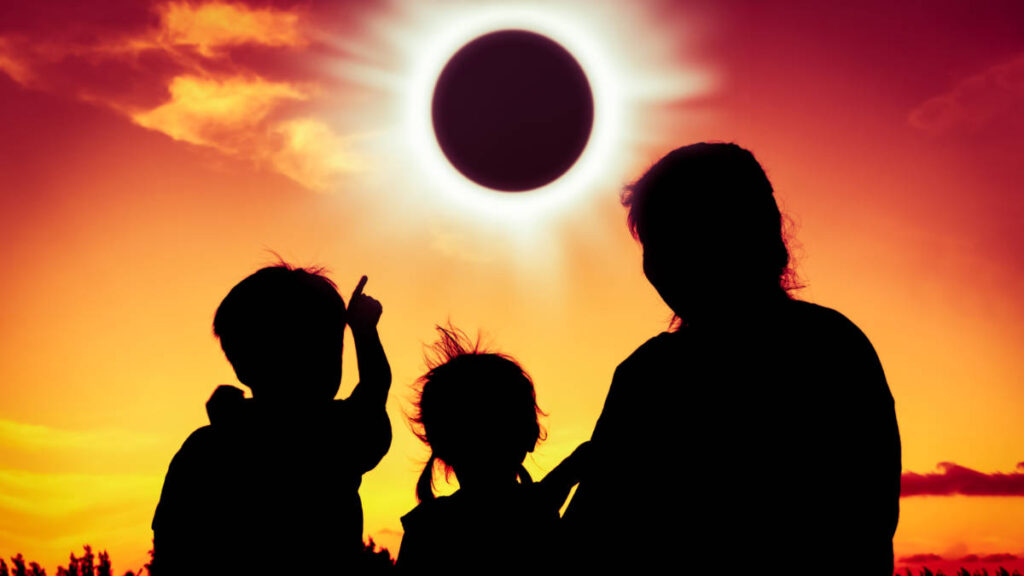 A silhouette of a mother with her children pointing the the solar eclipse on golden sky, Texas total solar eclipse April 2024