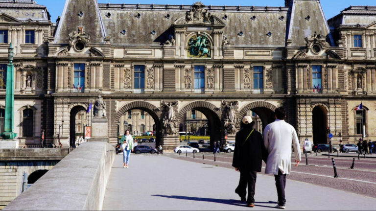 A couple walk along Pont du Carrousel towards Louvre Palace in Paris