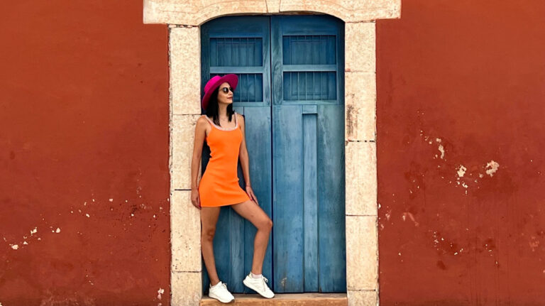 Clara stands against a blue door and red wall in Valladolid