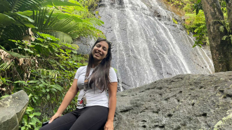 The author Vanessa Ramos sitting on a big rock with the La Coca Waterfall in the background