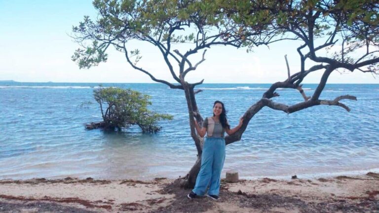 The author Vanessa Ramos, smiling or a photo at a beach next to a tree